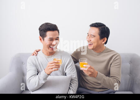 Two men clink glasses of whiskey at home, on the couch Stock Photo