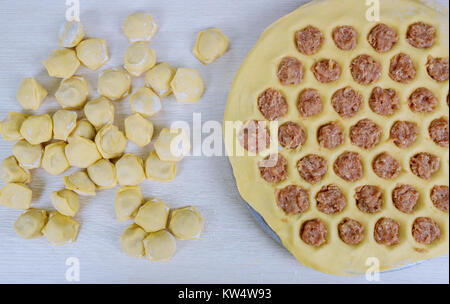 Process of making pelmeni, ravioli or dumplings with meat. Uncooked ukrainian russian pelmeni on cutting board and ingredients for homemade pelmeni on Stock Photo
