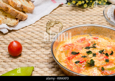 Close up of traditional Turkish dish "menemen" cooked with eggs, green pepper, and tomatoes in a copper pan and toasted sliced bread on a rustic table. Stock Photo