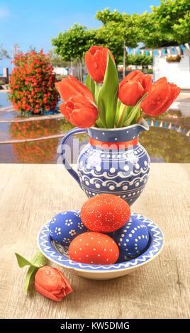 Blue ceramic vase with tulips and matching plate with painted Easter Eggs on a wooden table Stock Photo