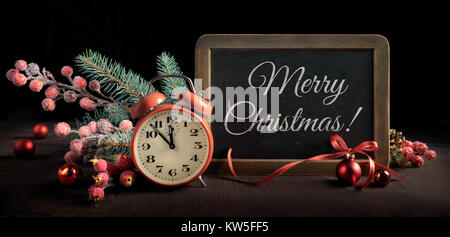 Blackboard with text "Merry Christmas" with alarm clock and Christmas decorations on black background. Panoramic framing for banner or web design. Ton Stock Photo