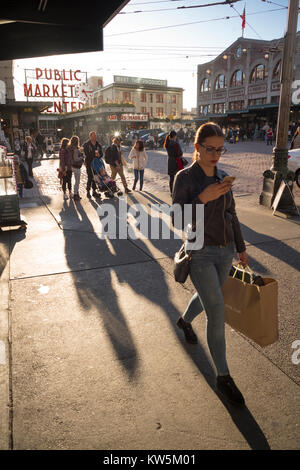 Young woman walking while looking at her cell phone, Pike Place Market, Seattle, Washington, USA Stock Photo