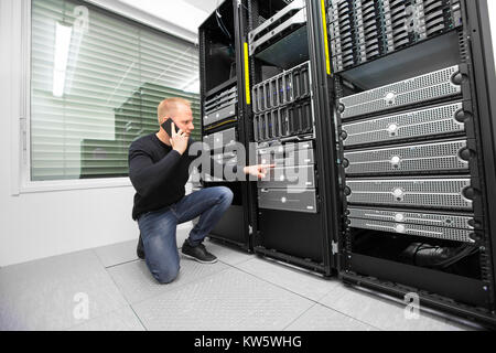 Consultant Using Smartphone While Monitoring Servers In Datacent Stock Photo