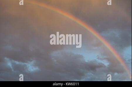 Rainbow in the stormy sky after the rain, lit by the rays of the sun. Stock Photo