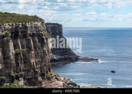 A small fishing boat moored at the base of North Head cliffs at the entrance to Sydney Harbour, Australia Stock Photo
