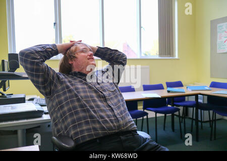 A young man relaxing in a chair at the front of a classroom Stock Photo