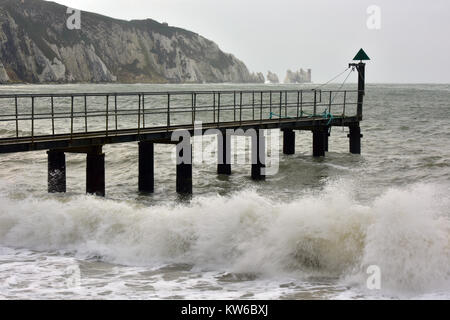 a pier or jetty at alum bay on the isle of wight being battered by rough seas and the needles lighthouse beyond. Waves crashing onto the shore. Stock Photo