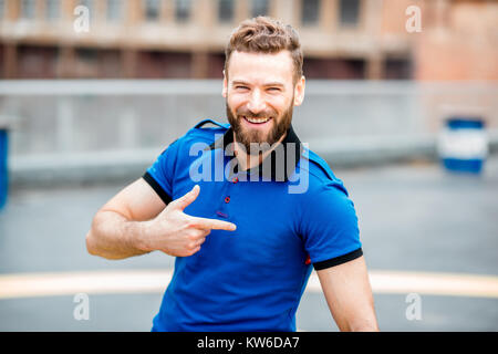 Lifestyle portrait of a handsome man pointing on a t-shirt standing outdoors on the helicopter platform Stock Photo