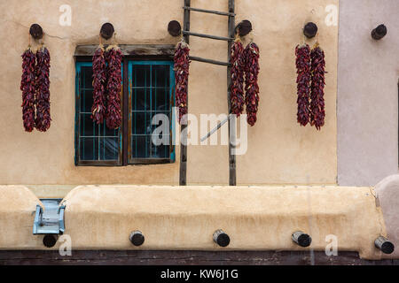 Red chili pepper ristras hanging on adobe buildings, Taos, New Mexico Stock Photo
