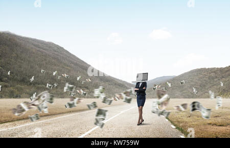 Business woman in suit with laptop instead of head keeping arms crossed while standing on the road among flying dollar banknotes with beautiful landsc Stock Photo