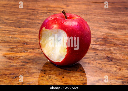 close up of red wet apple with a bite on rustic wooden table Stock Photo