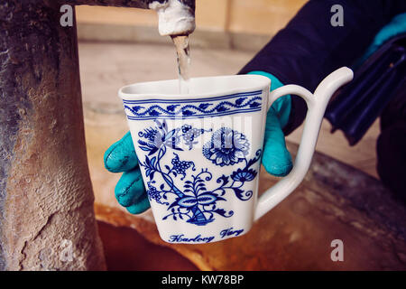 Hand in glove filling a cup with therapeutic mineral water at a natural hot spring in Karlovy Vary during winter time, Czech Republic Stock Photo