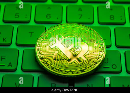 Gold Plated Iron Bitcoin on laptop keyboard with green neon light. Mining Stock Photo