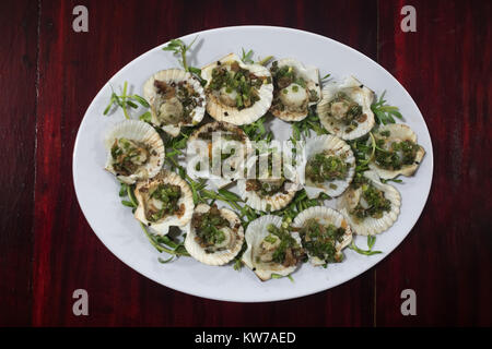 Grilled scallops with lemon, cilantro and white wine on white plate on wooden table. Stock Photo
