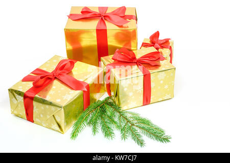 Concept of luxury Christmas gifts - boxes packed in golden paper and tied with a red satin ribbon next to branches on a white background Stock Photo