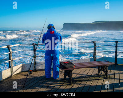 Sea Angler fishing from Saltburn Pier in North Yorkshire on a sunny winter day with a rough sea bringing large waves Stock Photo