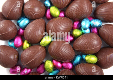 Pile of foil wrapped & unwrapped chocolate easter eggs in pink, blue & lime green, against a white background. Stock Photo