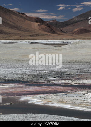 High mountain desert: the blue river flows through the white salted earth, in the background the brown mountains, Himalayas. Stock Photo