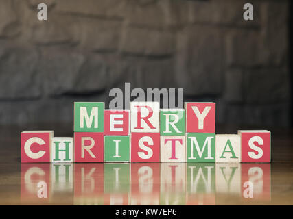Wood blocks in green, red and light wood with capital letters spelling Merry Christmas. Photographed with a shallow depth of field on a shiny wood tab Stock Photo