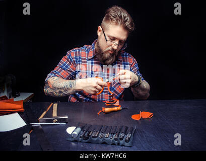 Artisan working with leather processes a workpiece from leather at his place of work Stock Photo