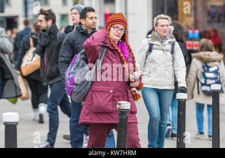 Woman wearing hand knitted colourful woolen chullo hat with braided earflaps in Winter in the UK. Stock Photo