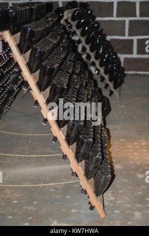 Traditional Champagne bottles being kept for secondary fermentation in the bottle in underground cellar. Méthode champenoise. Bottles in pupitres. Stock Photo