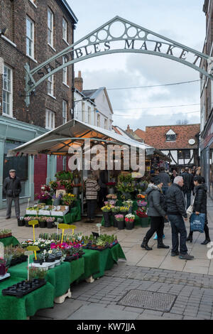 Centre of York with people walking past line of Shambles Market stalls & male trader serving a customer at his flower stall - Yorkshire, England, UK. Stock Photo