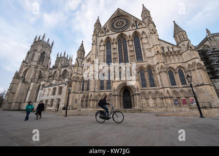 York centre - south entrance to magnificent York Minster from piazza where people walk & female on phone cycles past - North Yorkshire, England, UK. Stock Photo