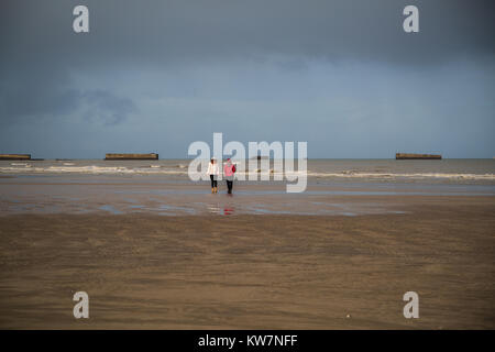 Walking along the beach at Arromanches les Bains with the remains of the Phoenix caissons in the background. Stock Photo