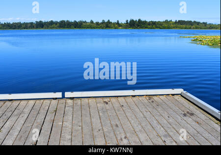 Beautiful tranquil Lake Terrell in the Pacific Northwest city of Ferndale, Washingon, USA.   A dock is in the foreground with evergreen trees lining Stock Photo