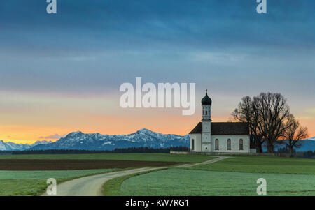 Sunrise over old chapel in green field with Alps mountains on background Stock Photo