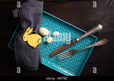 Table setting for festive Easter dinner decorated with easter bunny and eggs on dark wooden table Stock Photo