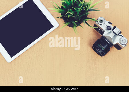 Concept of creative workplace - top view of retro slr camera, green flower and digital tablet on a wooden desk ( vintage effect) Stock Photo