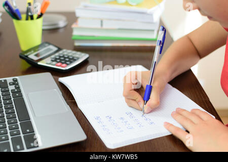 Young schoolgirl is doing a homework with math next to a laptop, calculator and books on her desk in her room Stock Photo