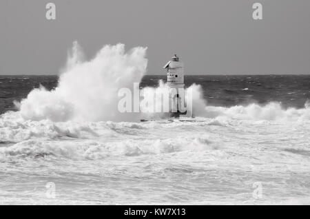 White lighthouse on the cliff. Lighthouse Mangiabarche situated in the south of Sardinia. Italy. Black and white, grey sky, white wave. Stock Photo