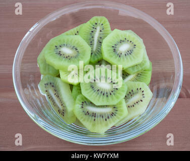 Bowl full with high in vitamins Kiwi fruit slices isolated on wooden background Stock Photo