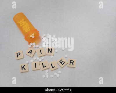 'Pain Killer' spelled with tan plastic tiles and black capital letters on stainless steel with an open orange prescription bottle of oxycodone tablets Stock Photo