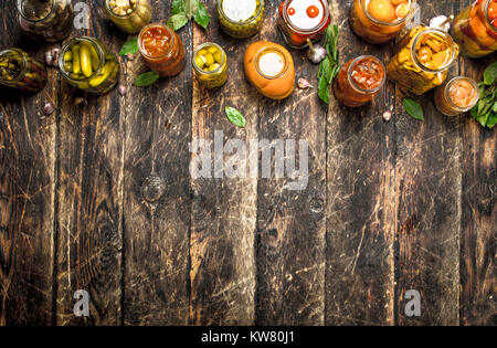 Different preserved vegetables from vegetables and mushrooms in glass jars. On a wooden background. Stock Photo