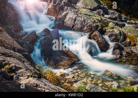 Beautiful waterfall in the mountains with the rays of the sun shining through the trees Stock Photo