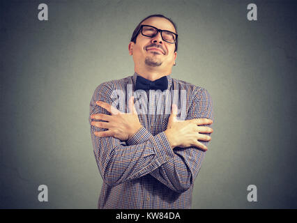 Young stylish man in bow-tie and eyeglasses embracing himself with great feeling of love. Stock Photo