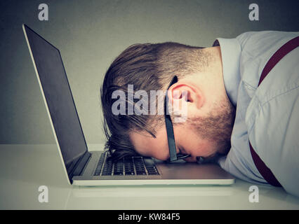 Side view of chubby man looking broken while lying on top of laptop. Stock Photo