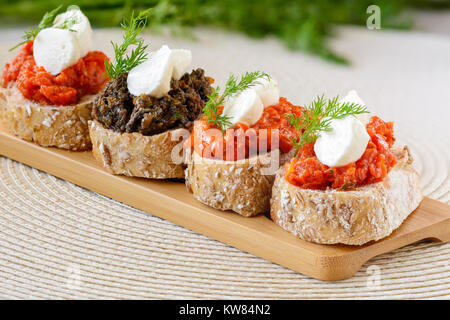 Appetizer bruschetta with mozzarella cheese, pepper-tomato paste, dried tomato paste with garlic and basil and  black olives paste with marinated cape Stock Photo