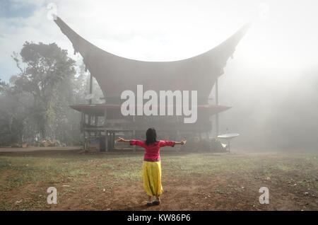 A woman standing in front of the Tongkonan house in Lolai. Lolai often known as 'Land Above the Cloud' or Negeri di Atas Awan in Banasa Indonesia. Stock Photo