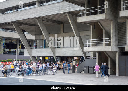 People sat outside the brutalist architecture of the National Theatre on London's South Bank, London, UK Stock Photo