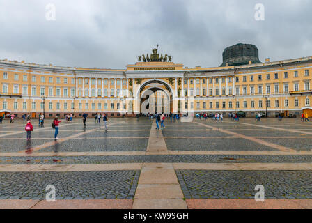 Unidentified tourists at Palace Square with the Arch of General Staff Building at the backgroud on a cloudy day. Saint Petersburg, Russia. Stock Photo