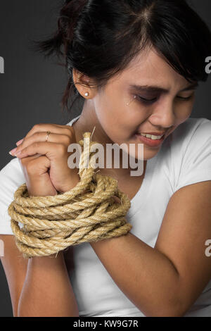 A portrait of a woman with hands tied up with rope being abused,   struggle, terrified,  and threaten from domestice violence and abuse Stock Photo