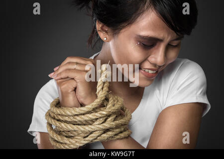 A portrait of a woman with hands tied up with rope being abused, struggle, terrified,  and threaten from domestic violence and abuse Stock Photo