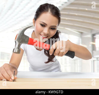 beauty young woman construction worker put nail on the wood using hammer Stock Photo