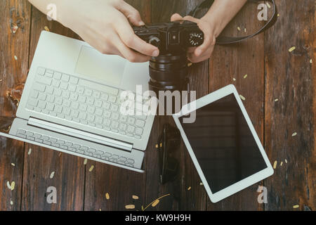Hipster vintage wooden desktop top view, male hands holding photocamera watching photos. Laptop and tablet is on table for work Stock Photo