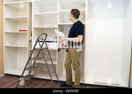 Worker with screwdriver inspecting new cabinet. Installation of furniture. Stock Photo